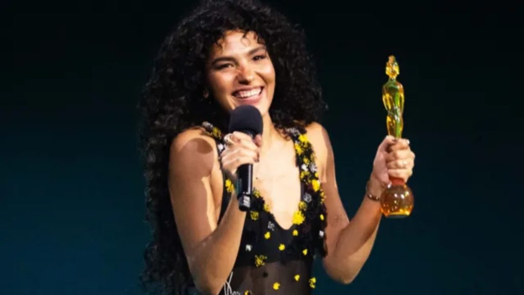 Olivia Dean smiling with Brit Award trophy at 2026 Brit Awards in black dress with yellow spots