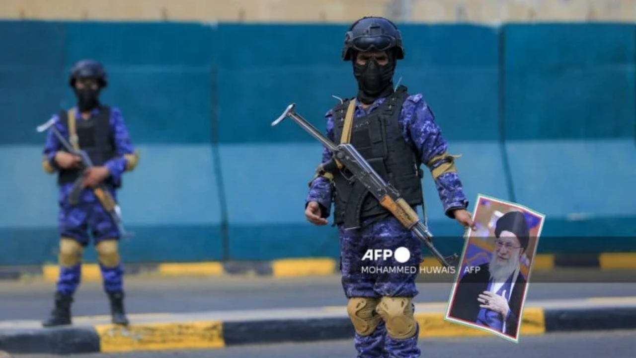 A masked fighter stands with a picture of Iran's supreme leader Ali Khamenei during a memorial rally held by supporters of Yemen's Huthis, a day after Khamenei was assassinated during US and Israeli strikes on Tehran, in the Huthi-held capital Sanaa on March 1, 2026