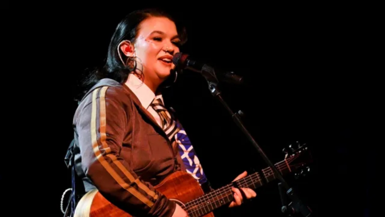 Lola Young performing on stage at London Palladium, playing acoustic guitar