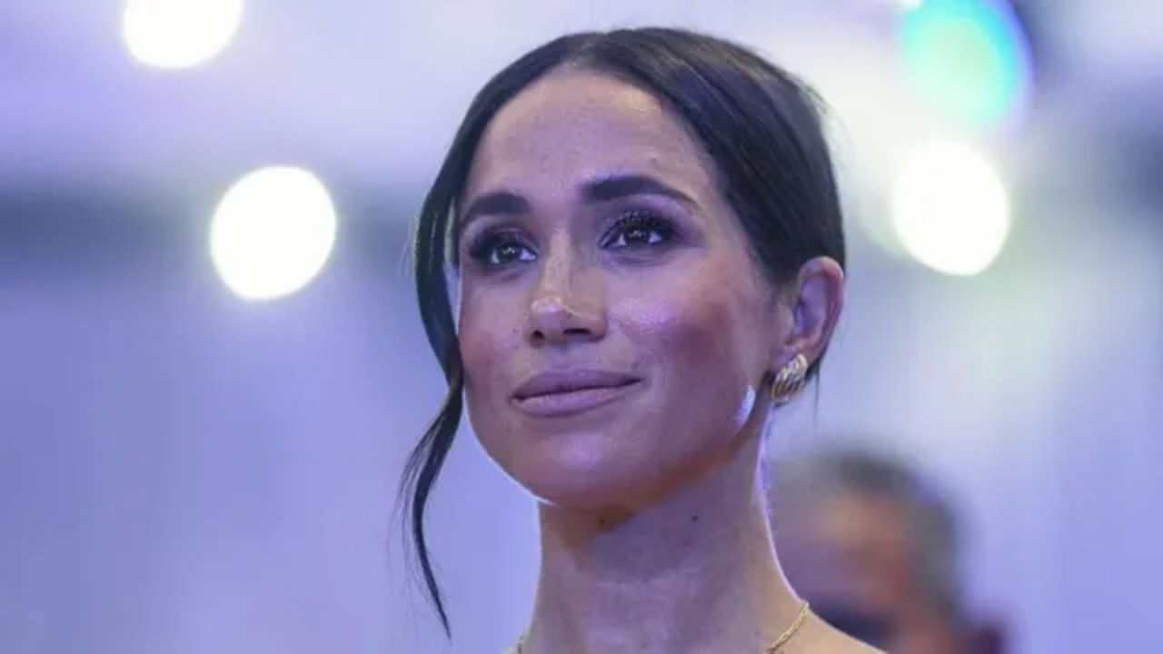 Meghan Duchess of Sussex smiling at a gala event with dark hair in an up-do and silver earrings