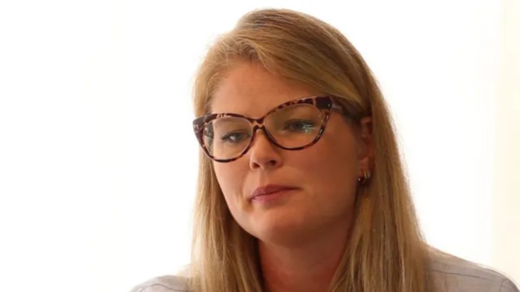 Gláucia Fekete, young Brazilian model, reflecting on past experiences, with long blonde hair and pale top.