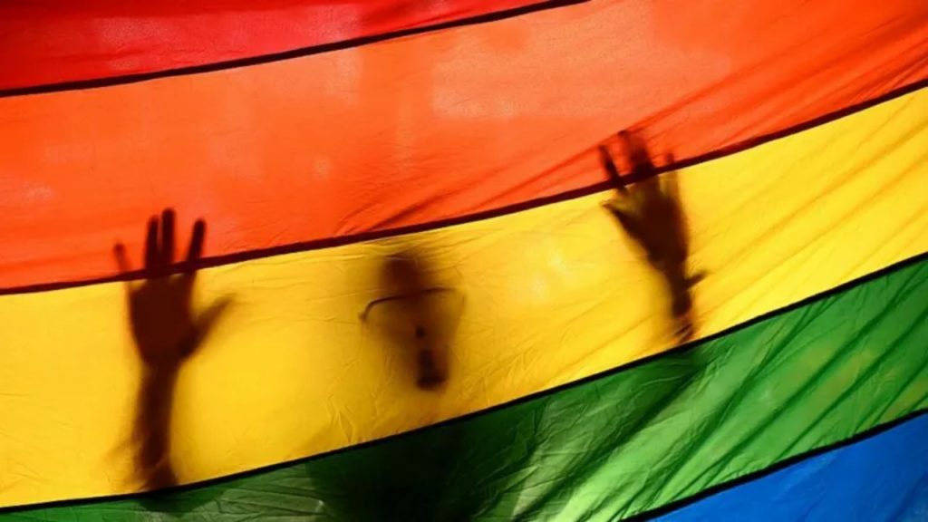 Silhouette of a person behind a rainbow LGBTQ+ flag representing debate over Senegal’s anti-gay law.