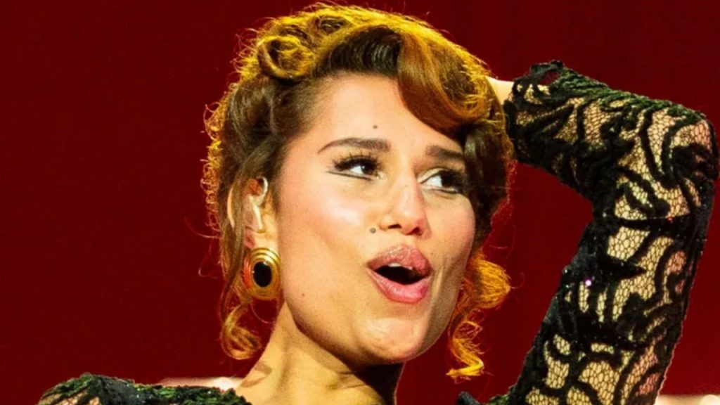 Raye performs on stage in a black ballgown, smiling under bright lights - National News