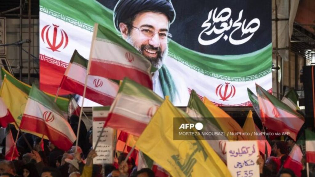 Pro-government demonstrators wave national flags, flags of Lebanon's Hezbollah, and a placard with Persian script reading, ''The Kohgiluyeh Lur hunter of F-35,'' in front of a portrait of Iran's new Supreme Leader Ayatollah Mojtaba Khamenei, during the funeral ceremony for Majid Khademi, head of Iran's IRGC Intelligence Organization, in Tehran, Iran, on April 8, 2026 - National News